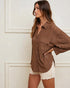 Woman wearing a brown textured jacket and white shorts against a white wall.