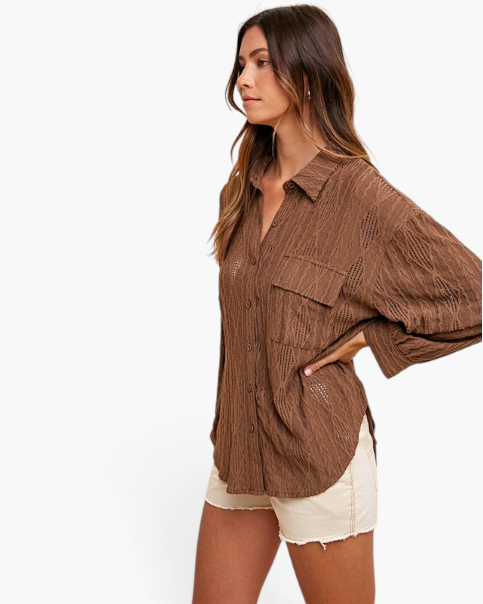 A woman wearing a brown textured button-up shirt with cream shorts, photographed against a plain white studio background.