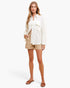 A woman modeling a white textured button-up shirt and beige shorts against a clean white studio background.