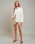 Woman wearing a white blouse and beige shorts on a plain background