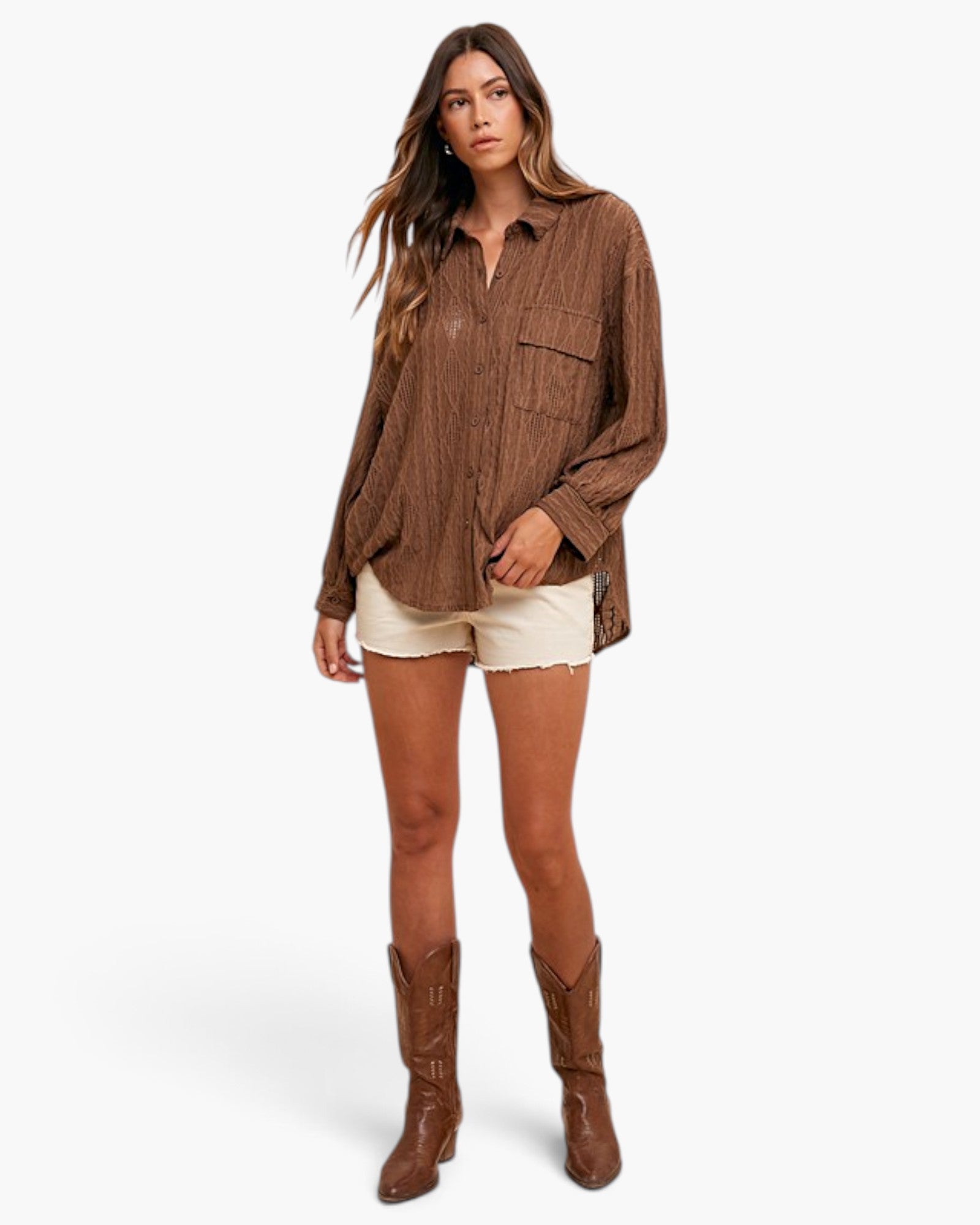 A woman modeling a brown textured button-up shirt with cream denim shorts and brown leather cowboy boots, photographed against a clean white studio background.