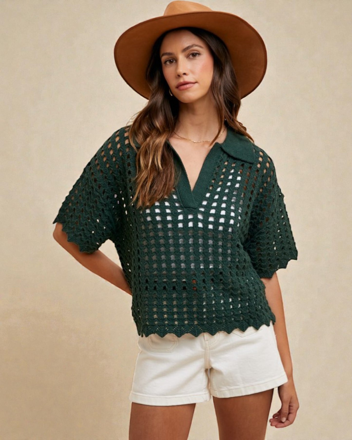 Woman wearing a green crochet top and white shorts with a brown hat on a beige background