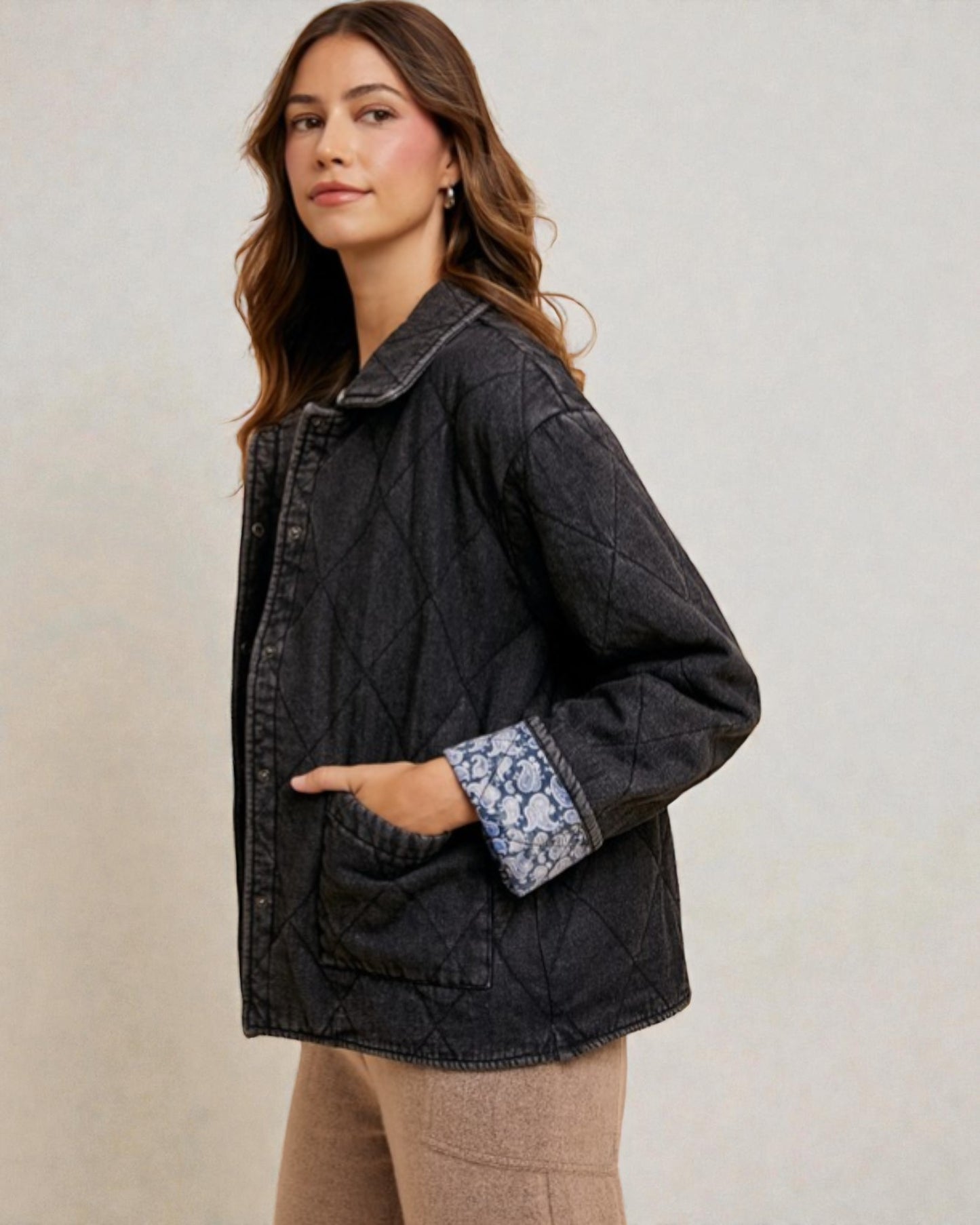 Woman wearing a black quilted jacket with floral cuffs on a plain background