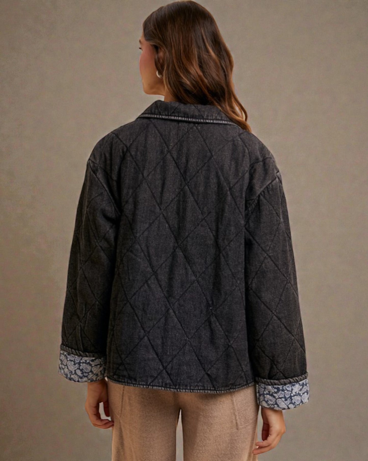 Person wearing a quilted dark jacket with floral cuffs on a beige background