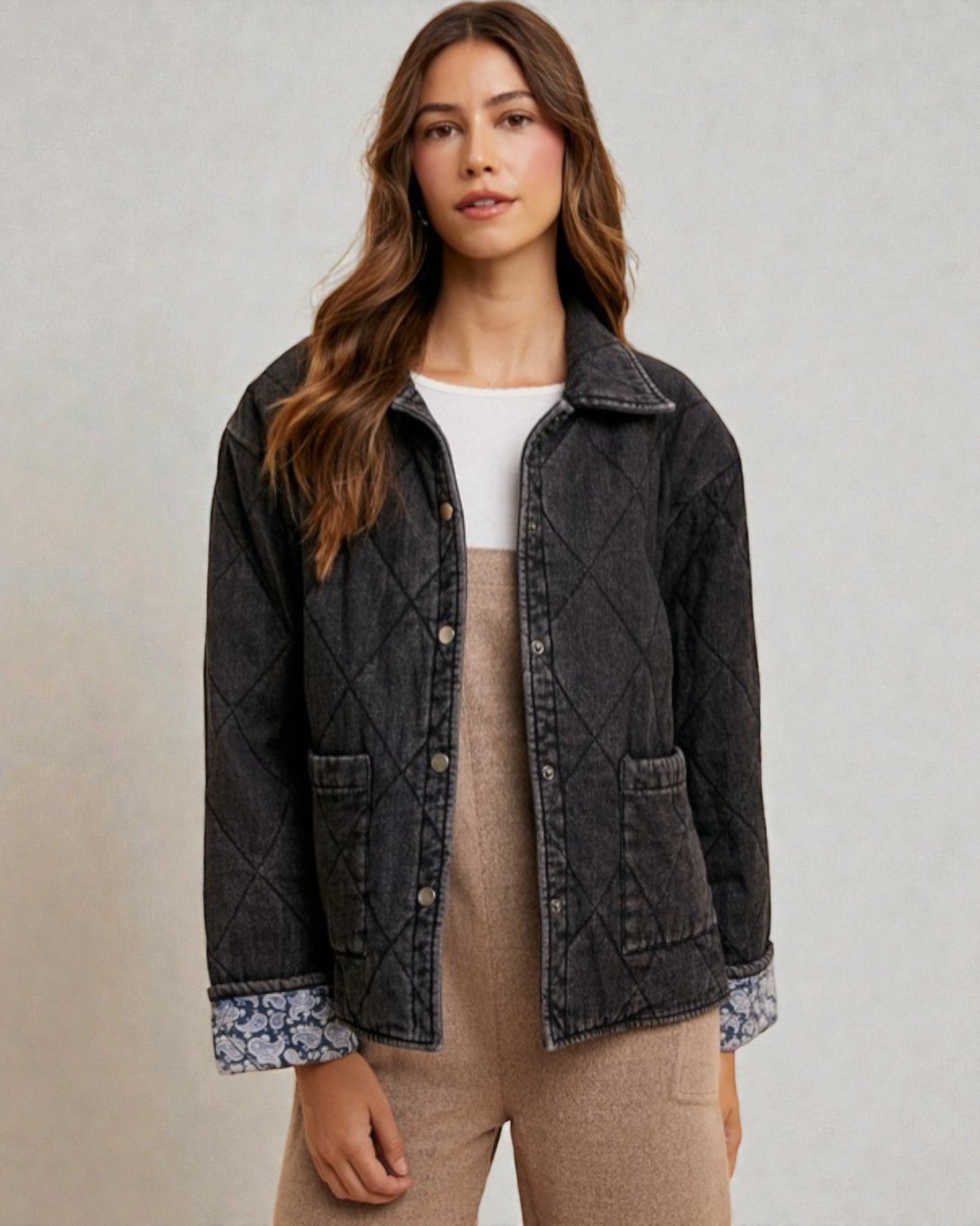 Woman wearing a dark denim jacket over a white shirt and beige pants on a neutral background