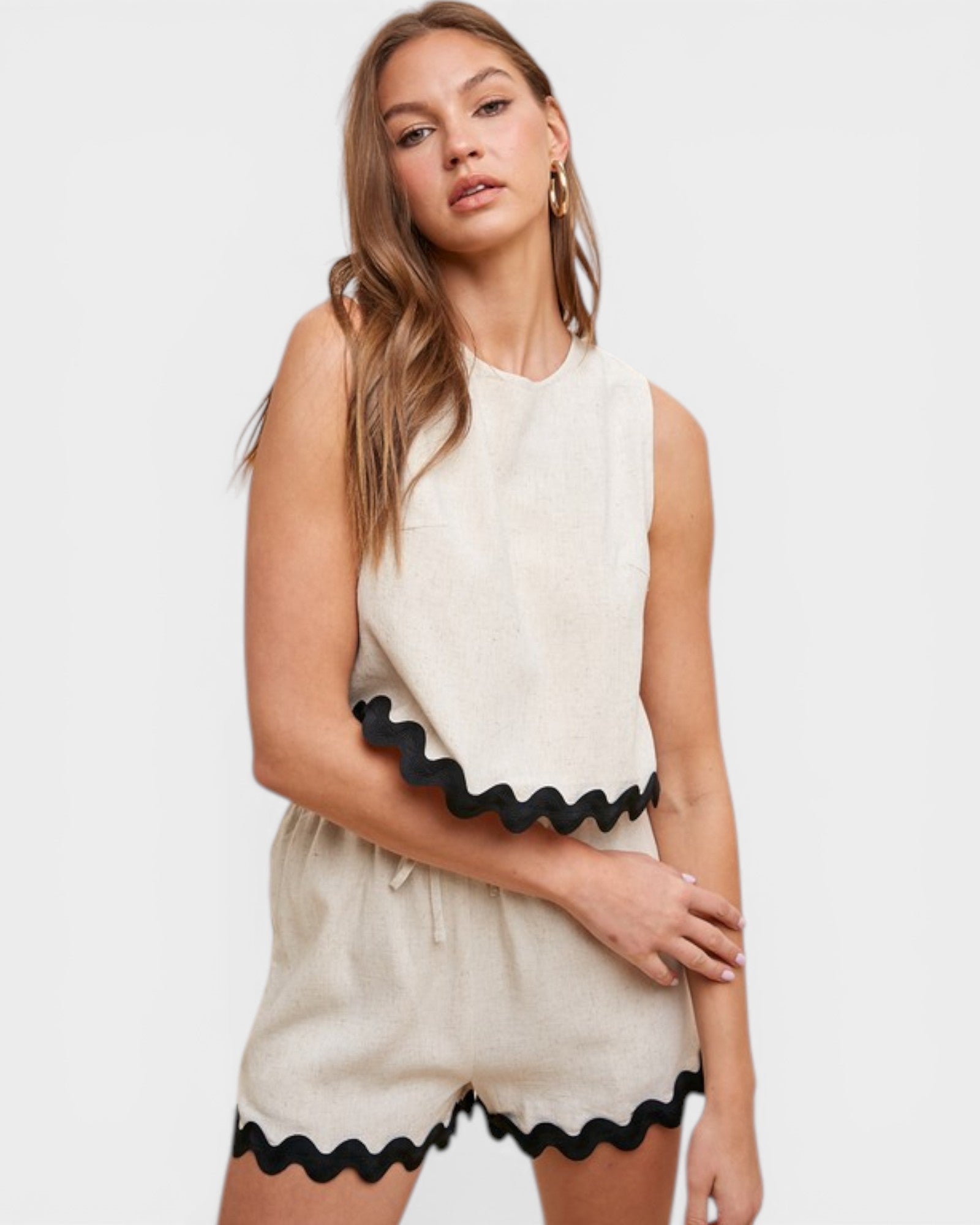 Woman wearing a white sleeveless top and shorts with black trim on a white background