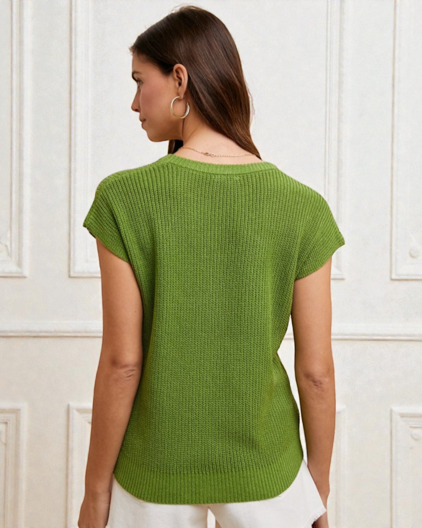 Woman wearing a green knitted top against a white paneled wall