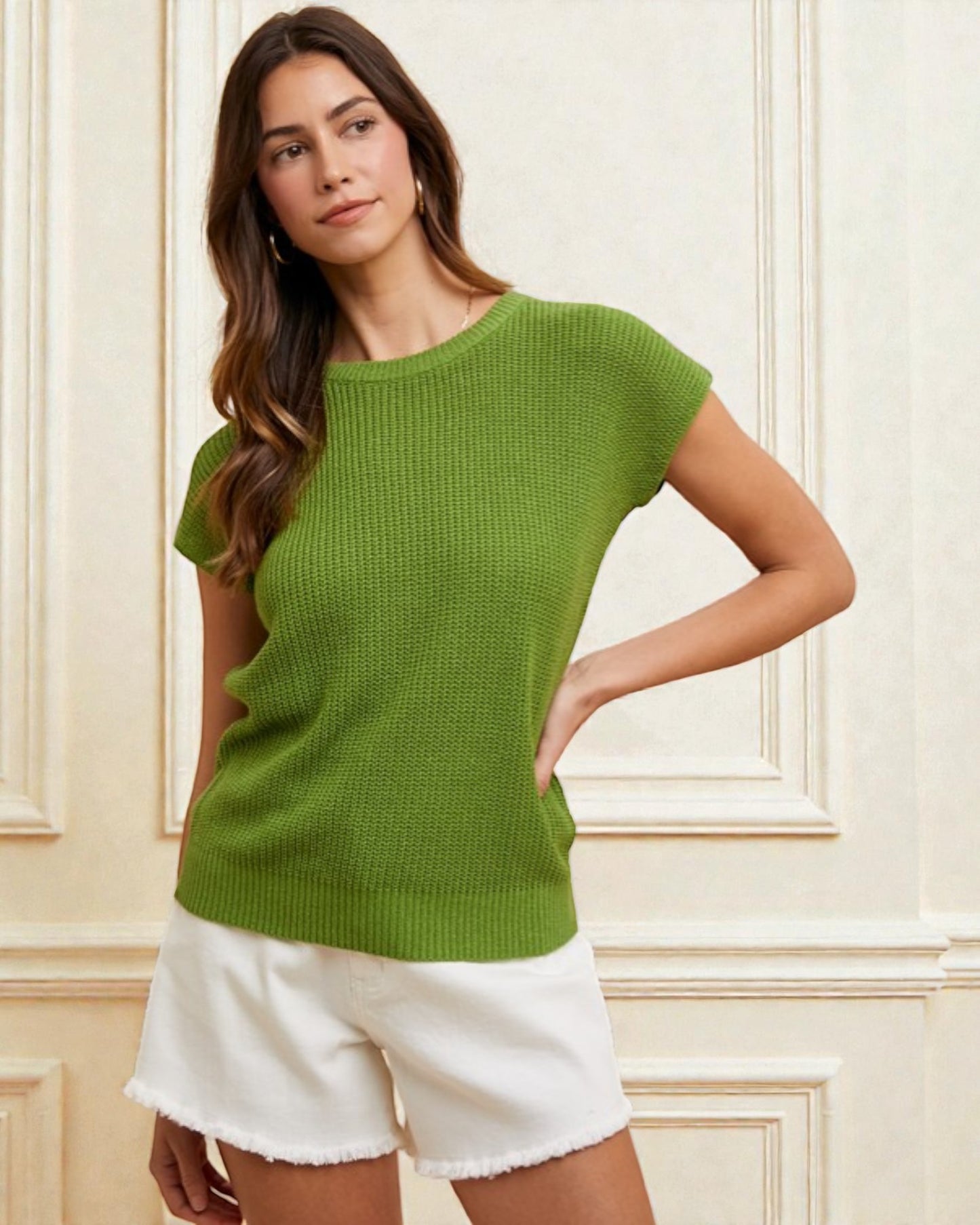 Woman wearing a green sweater and white shorts against a light-colored wall.