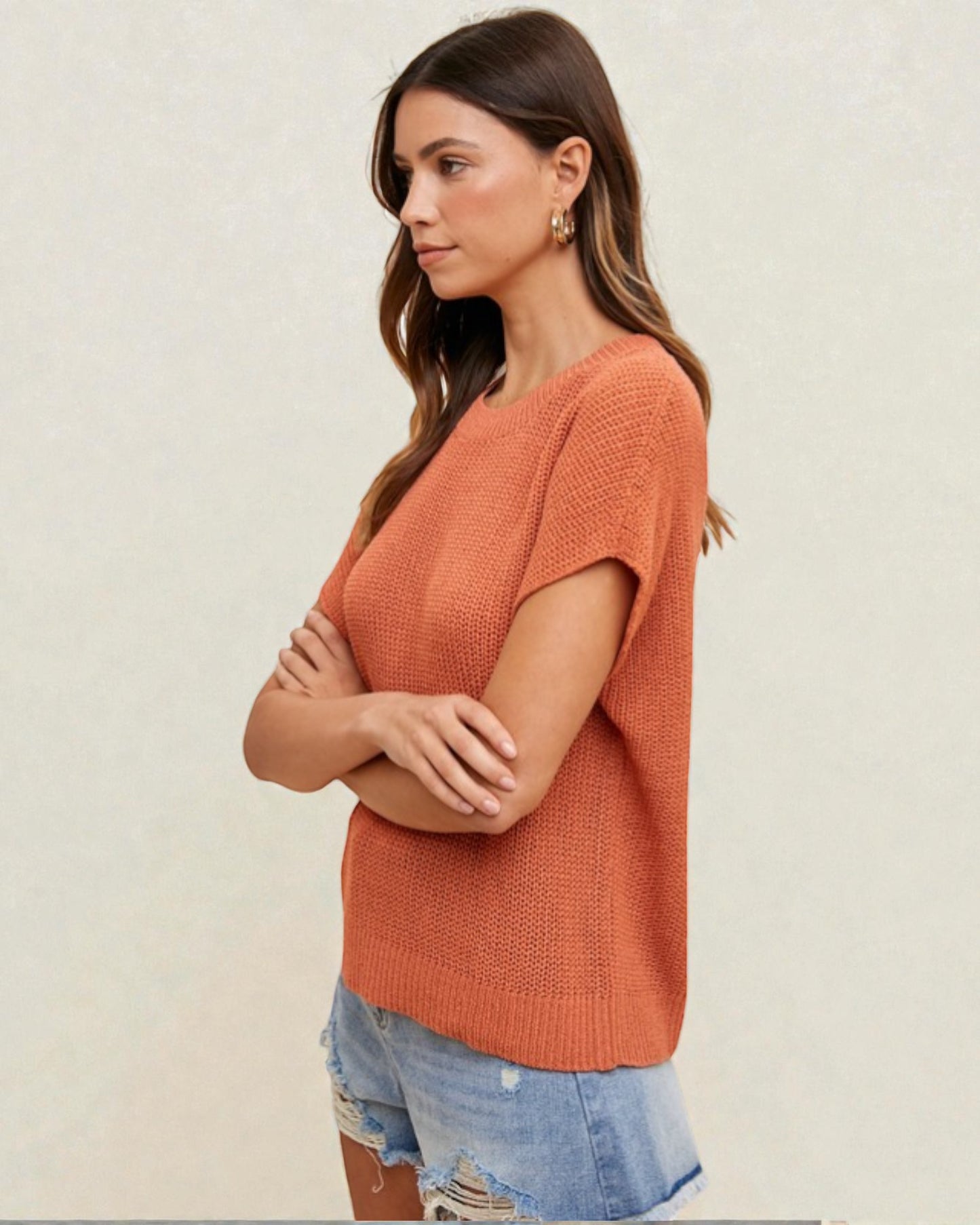 Woman wearing a rust-colored knit sweater with denim shorts on a plain background
