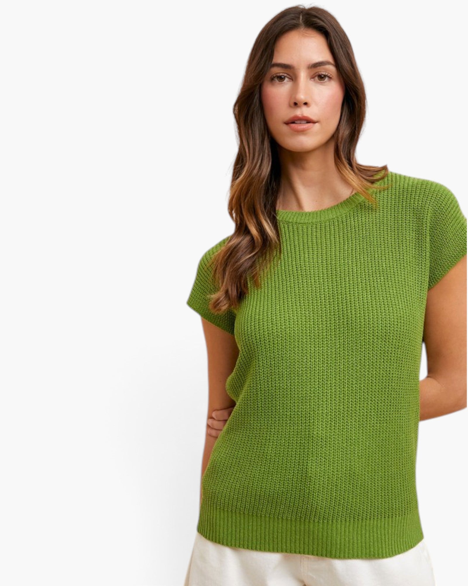 A woman wearing a bright green short-sleeve knit top with a textured waffle pattern, paired with off-white pants, against a plain white background.