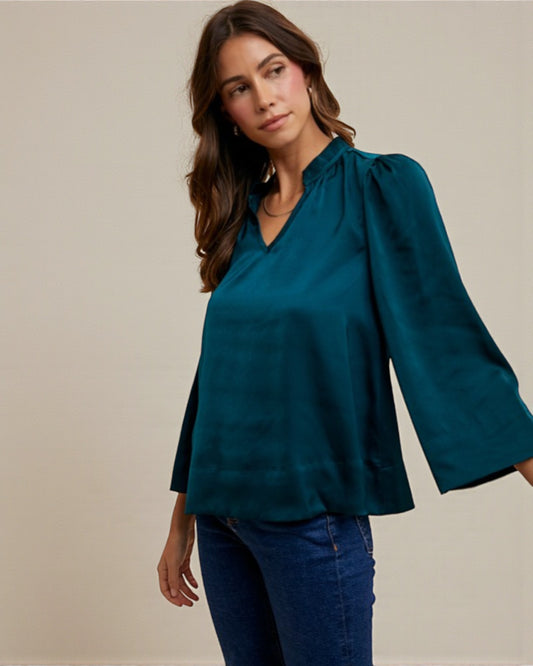 Woman wearing a teal blouse with long sleeves against a beige background
