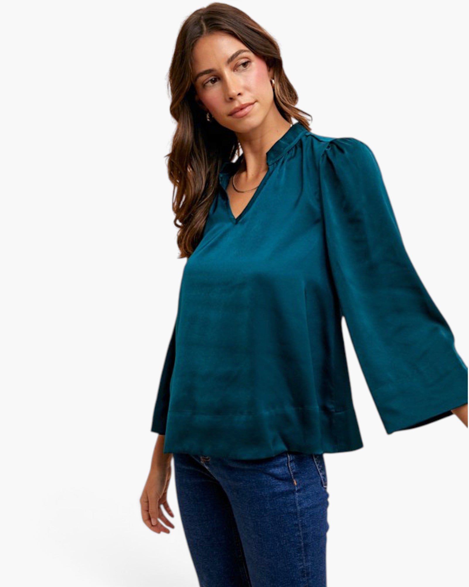 A woman wearing a teal long-sleeve blouse with puff sleeves and a split neckline, paired with blue jeans, against a plain white background.
