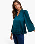 A woman wearing a teal long-sleeve blouse with puff sleeves and a split neckline, paired with blue jeans, against a plain white background.