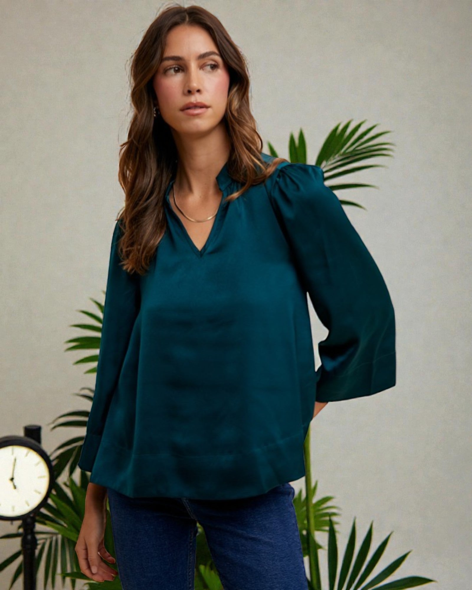 Woman wearing a teal blouse standing in front of a plant