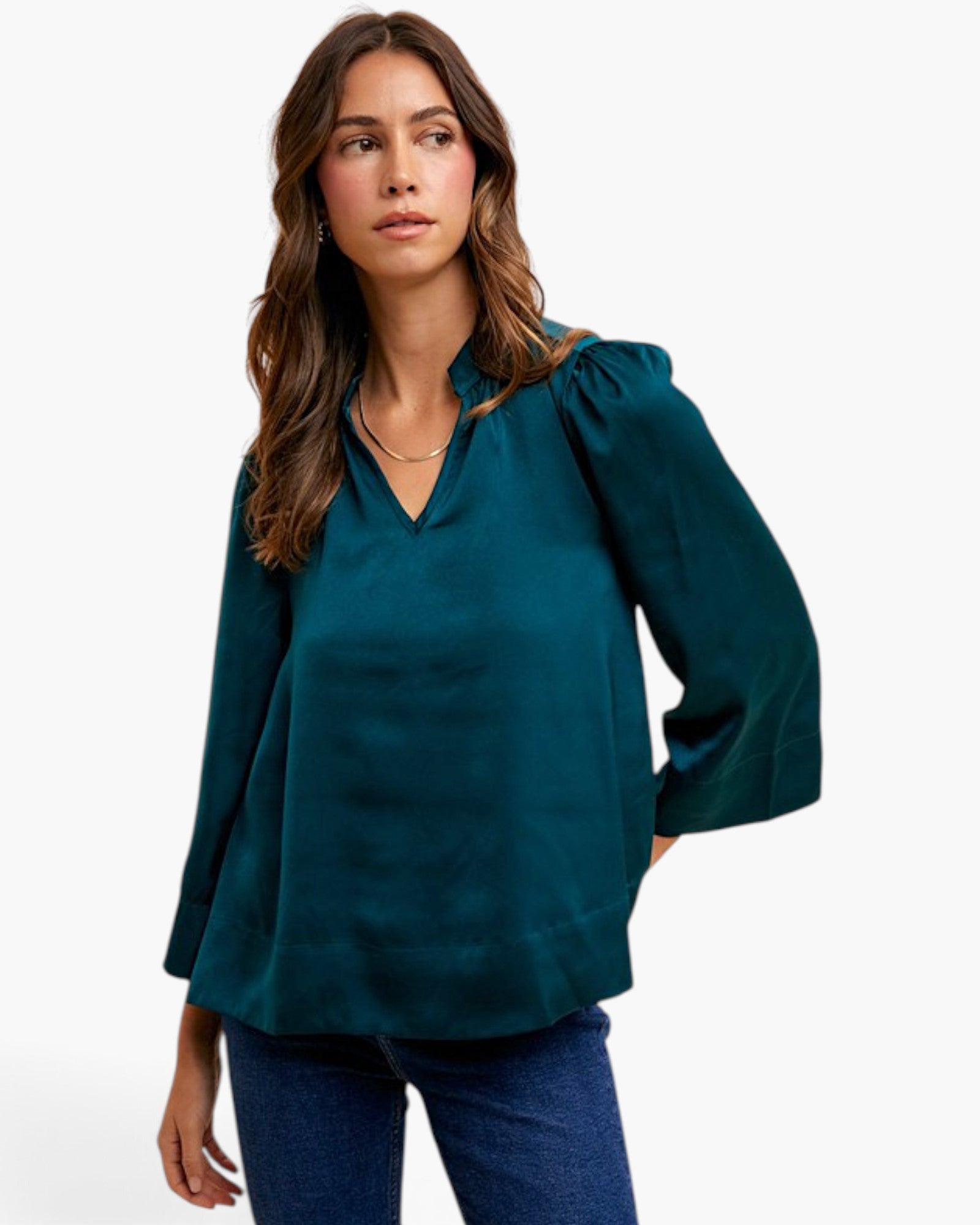 A woman wearing a dark teal blouse with puffed shoulders and a split V-neckline, paired with blue jeans, photographed against a clean white studio background.