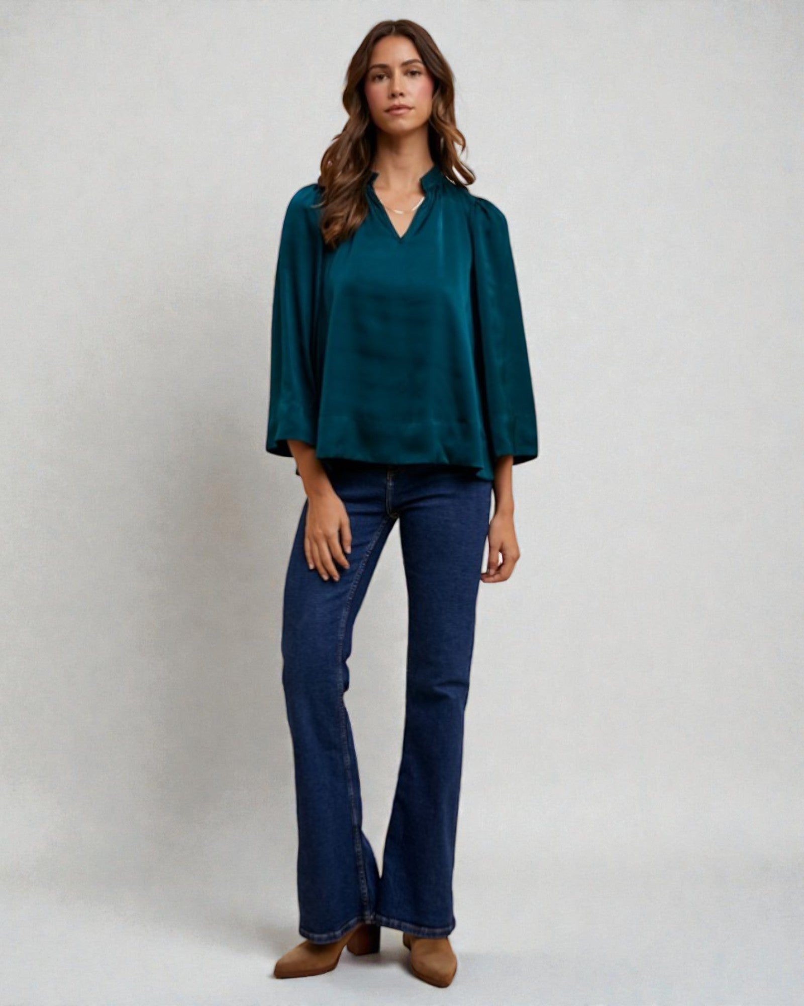 Woman wearing a teal blouse and blue jeans on a white background