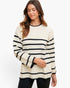 A woman wearing a cream-colored knit sweater with horizontal black stripes, paired with black pants, against a plain white studio background.