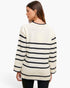 A woman shown from the back wearing a cream knit sweater with horizontal black stripes and black ribbed trim, paired with black pants, against a plain white studio background.