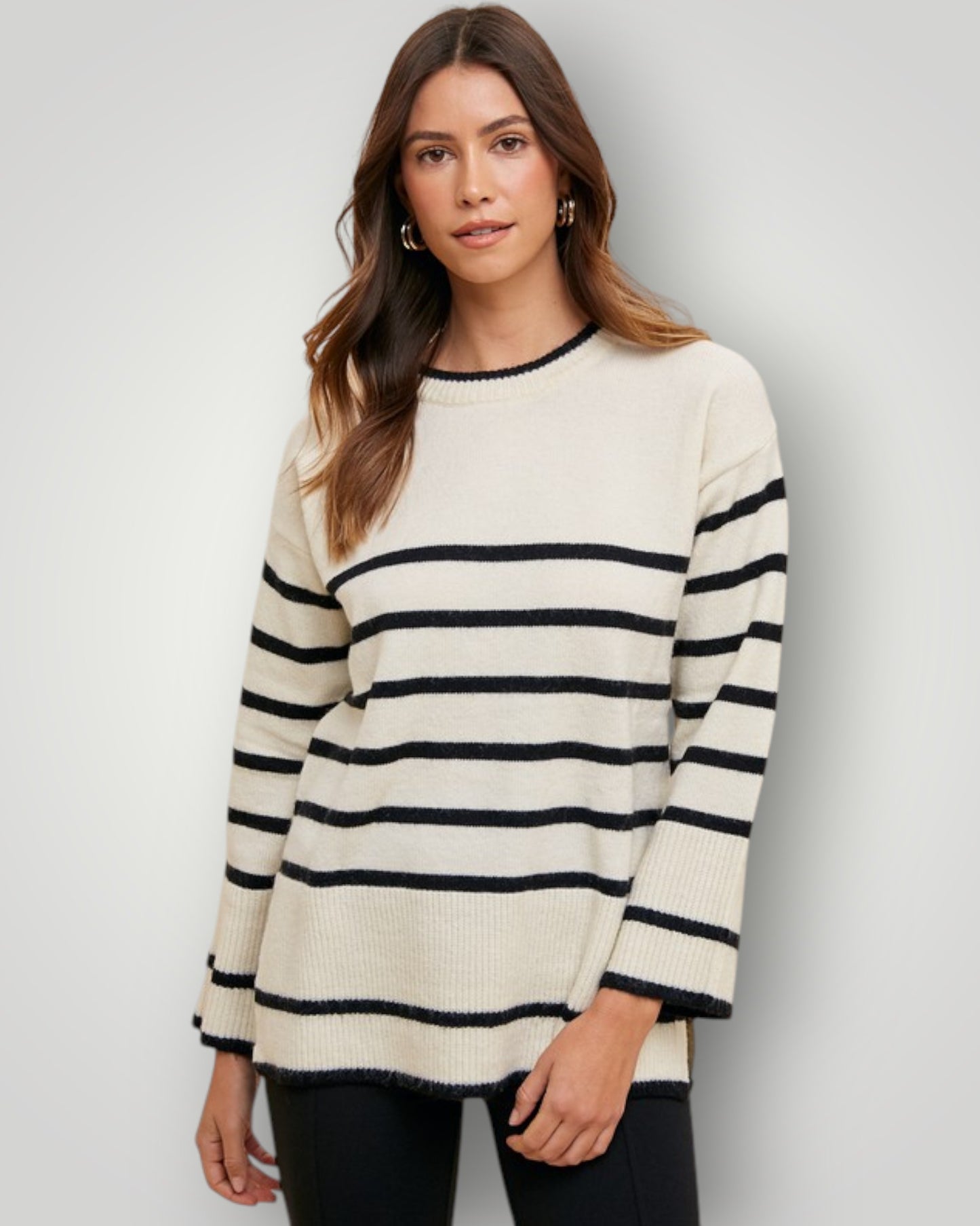 Woman wearing a cream and black striped sweater on a plain background