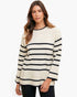 A woman wearing a cream-colored knit sweater with horizontal black stripes and black pants, photographed against a clean white studio background.