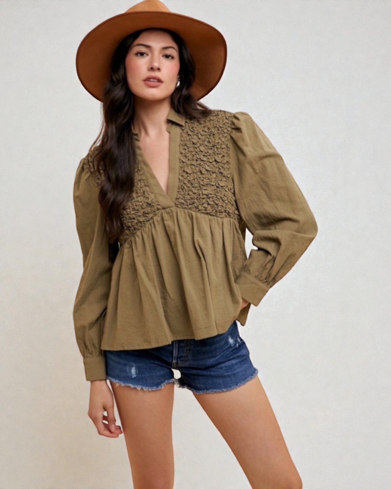 Woman wearing a brown hat, green blouse, and denim shorts on a white background