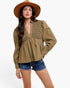 A woman modeling a long-sleeve olive green blouse with a lace-trimmed V-neck and peplum waist, paired with denim shorts and a wide-brim tan hat against a light gray studio background.