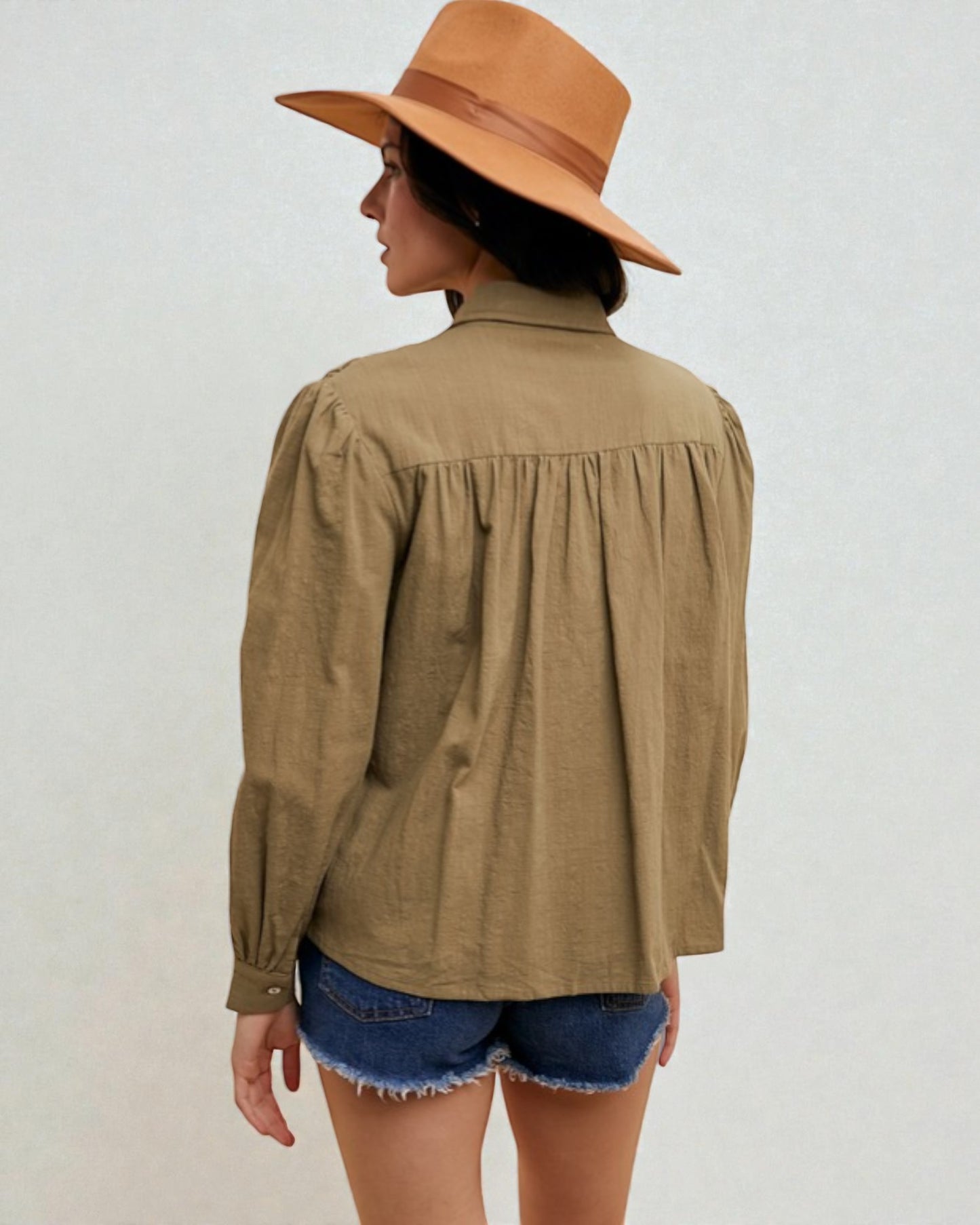 Person wearing a brown hat and olive green shirt with denim shorts on a white background