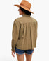 A woman shown from the back wearing a light brown long-sleeve blouse with gathered detailing at the shoulders and waist, paired with denim shorts and a tan wide-brim hat, against a plain white background.