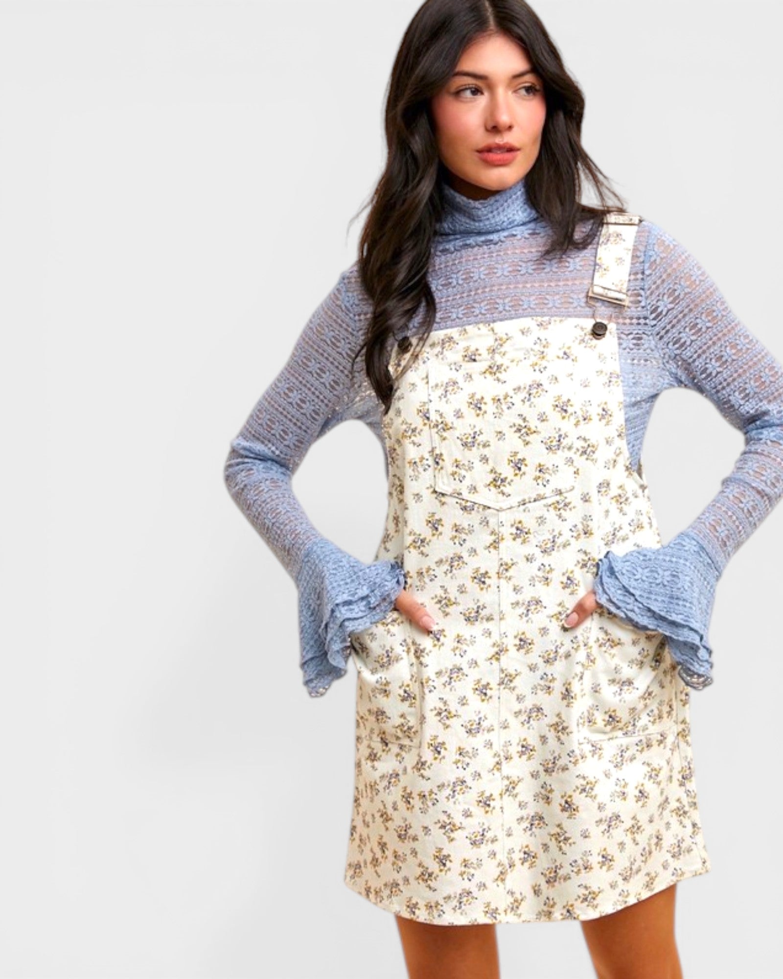 Woman wearing a floral dress over a turtleneck with blue sleeves on a white background
