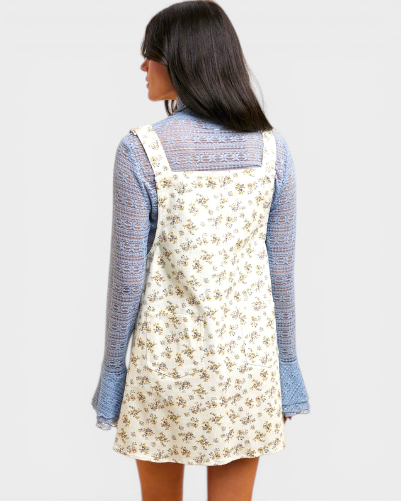 Woman wearing a floral pinafore dress over a blue sweater on a white background