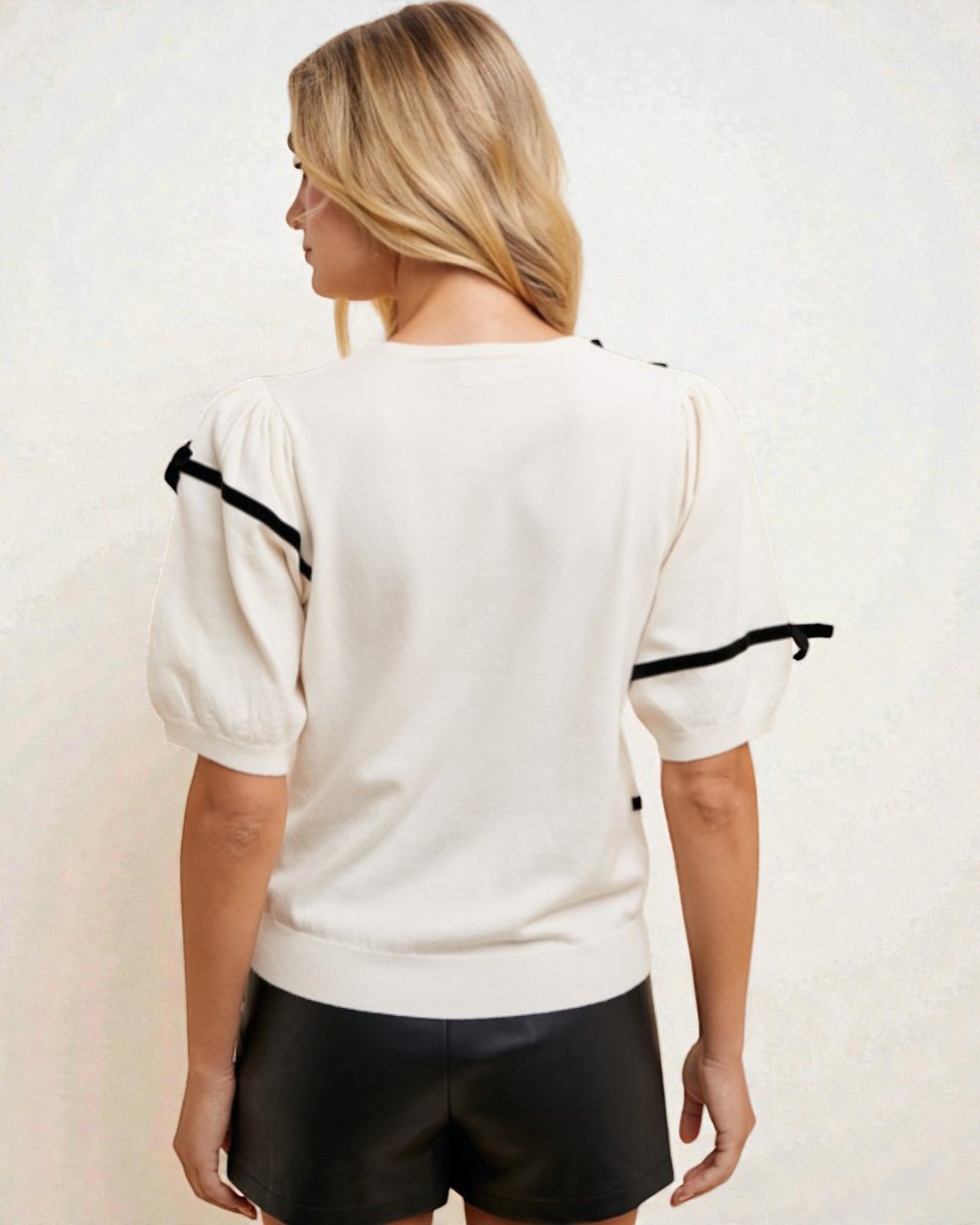 Woman wearing a white top with black accents on a plain background