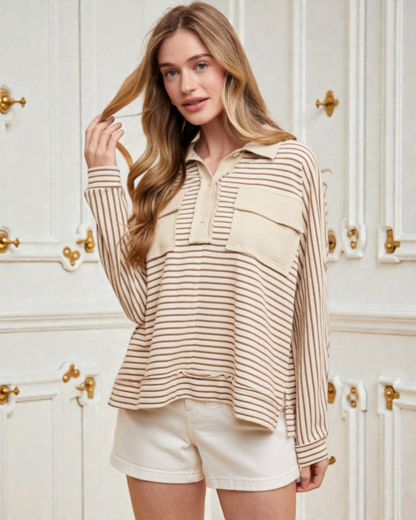 Woman wearing a striped shirt and shorts in a room with white walls and gold door handles.