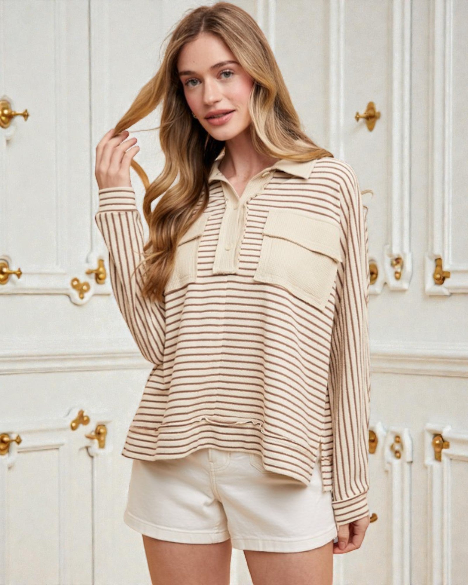 Woman wearing a striped shirt and shorts in a room with white walls and gold door handles.