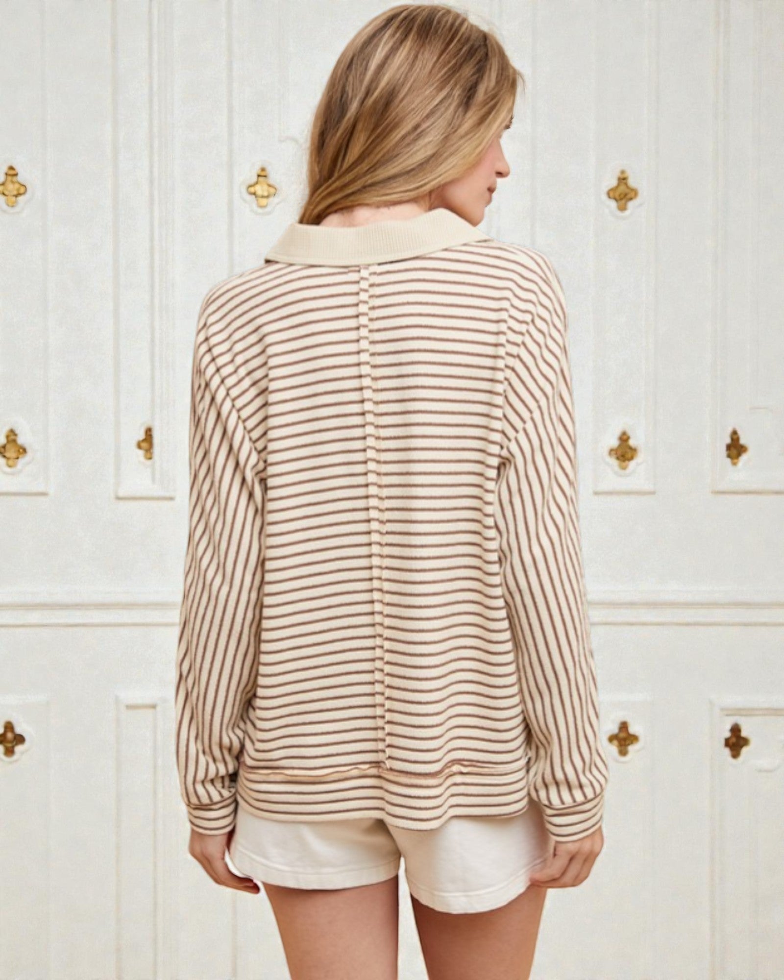 Woman wearing a striped shirt and shorts in front of a white wall with gold accents.
