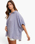 A woman wearing a loose, oversized button-up shirt with vertical blue and white stripes, styled with white shorts against a clean white background.