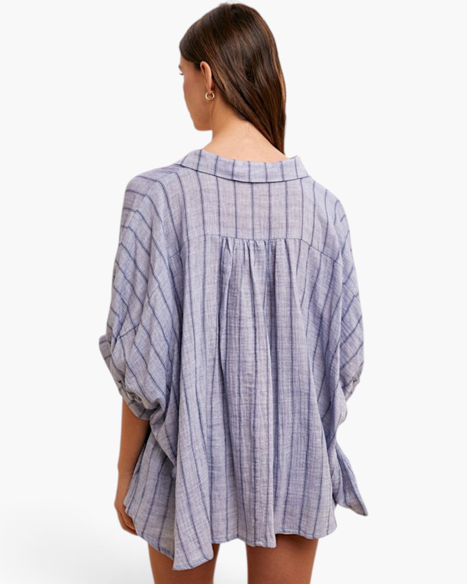 A woman shown from the back wearing a loose, oversized button-up shirt with a blue and white vertical stripe pattern, photographed against a clean white studio background.