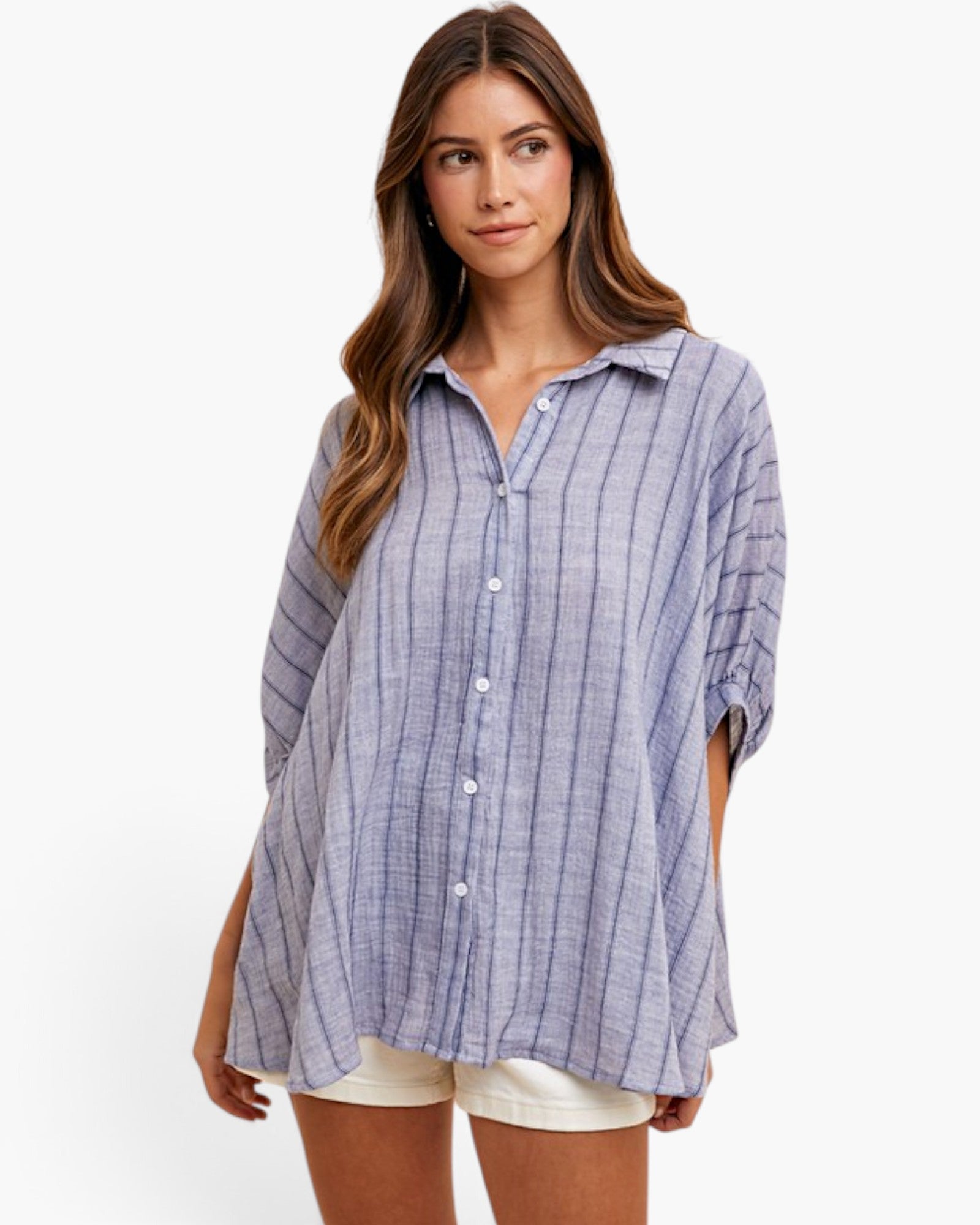 A woman modeling a loose, short-sleeve button-up shirt with a blue and white vertical stripe pattern, paired with white shorts, against a plain white studio background.