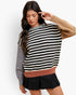 A woman modeling a color-block knit sweater with horizontal black and cream stripes across the chest and sleeves, a solid gray long sleeve, a tan long sleeve, and a dusty rose ribbed hem, paired with a black pleated mini skirt against a light gray studio background.