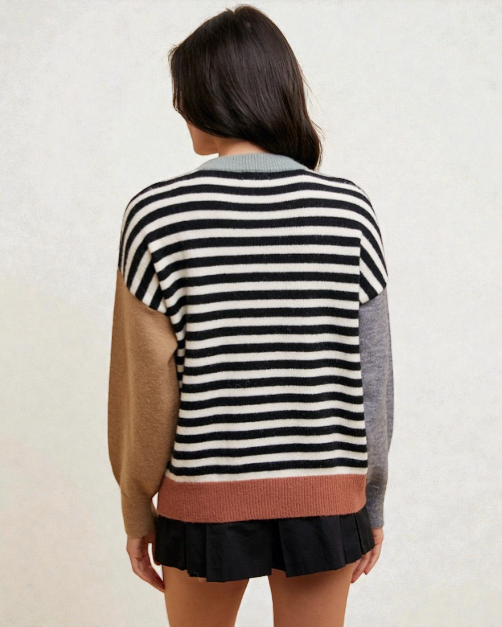 Person wearing a striped sweater with color-blocked sleeves on a plain background