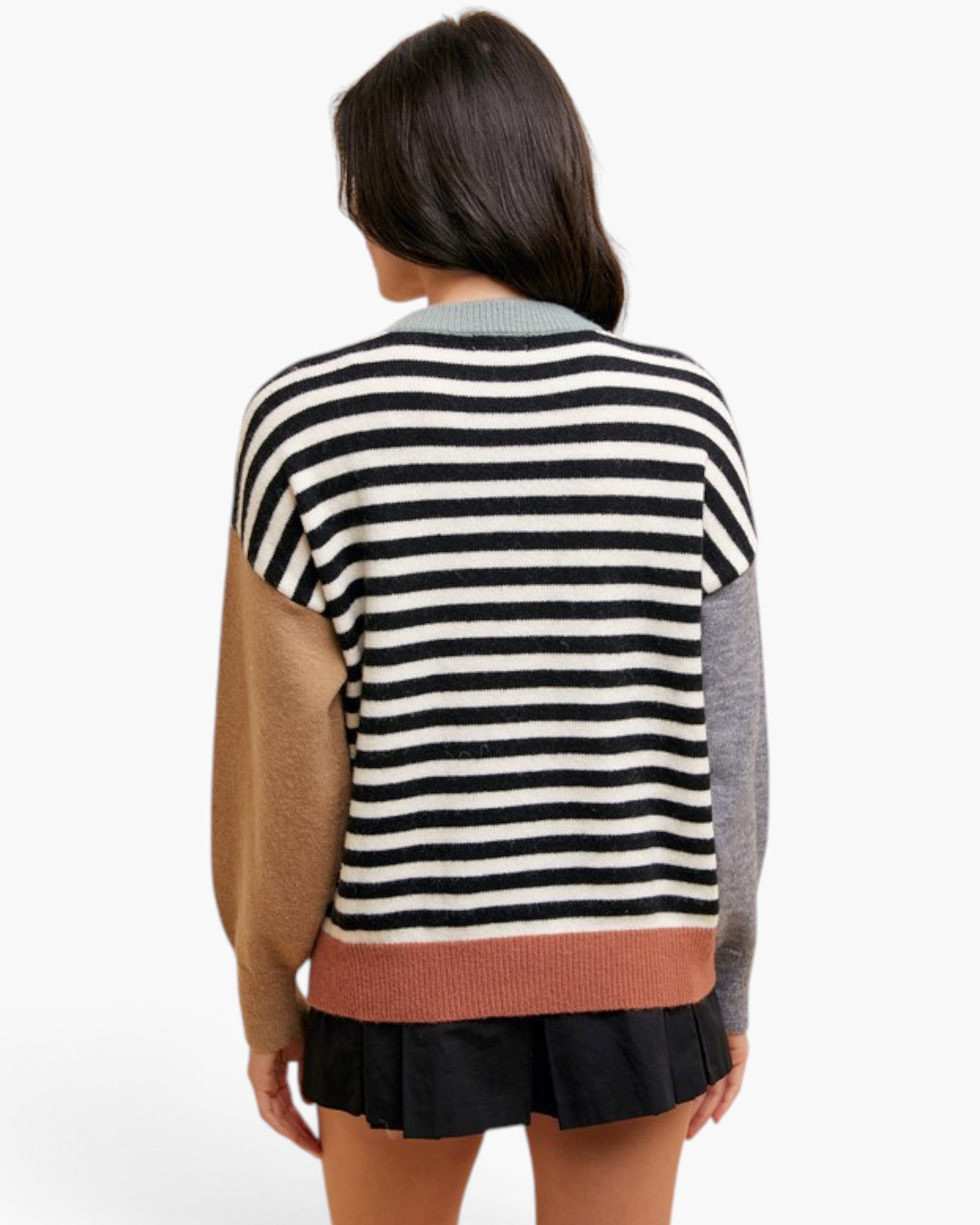 A woman shown from the back wearing a color-block knit sweater with horizontal black and off-white stripes across the upper body, tan sleeves, a heather gray sleeve, and a muted terracotta hem.