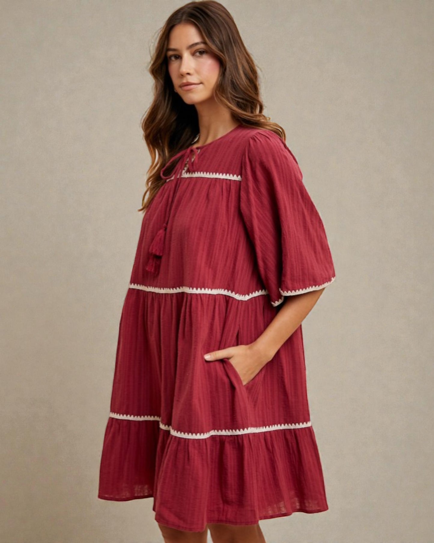 Woman wearing a burgundy dress with white trim against a beige background