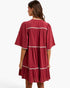 A woman shown from the back wearing a tiered, short-sleeved dress in a deep red or burgundy crinkle fabric with white embroidered trim details.
