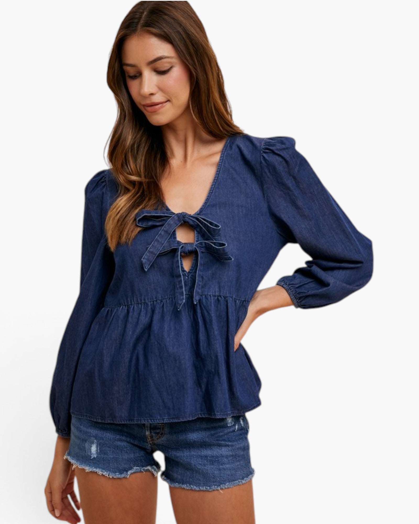 A woman wearing a dark blue denim long-sleeve blouse with a tie-front keyhole and puff sleeves, paired with denim shorts, against a plain white background.