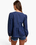 A woman shown from the back wearing a dark blue denim long-sleeve peplum top and matching denim shorts against a plain white background.