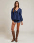 Woman wearing a blue top and denim shorts with brown knee-high boots on a plain background