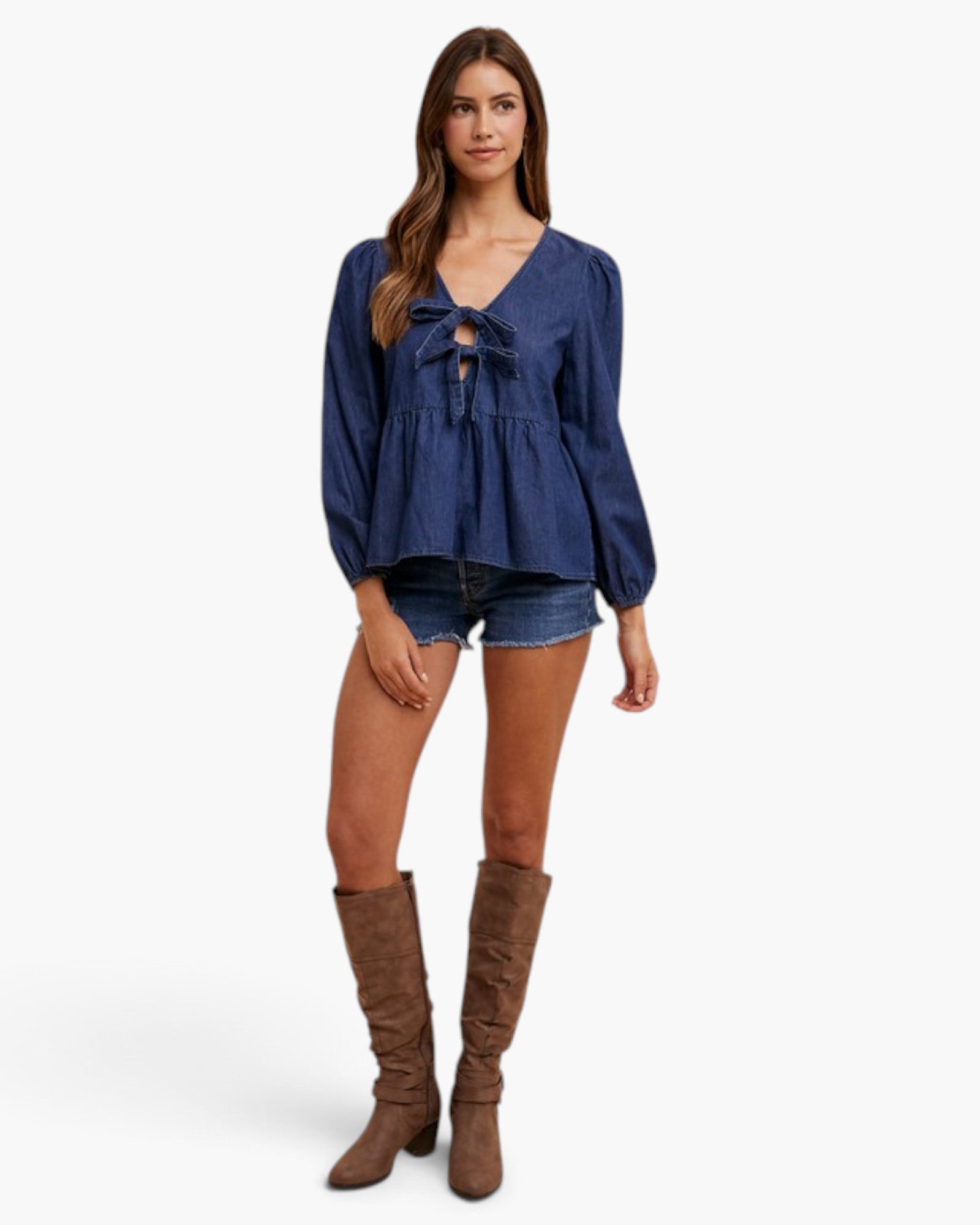 A woman modeling a blue long-sleeve tie-front blouse with denim shorts and brown knee-high boots against a light gray studio background.