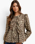 A woman wearing a beige and brown leopard-print long-sleeve blouse with ruffled details and a tie-neck bow, paired with blue jeans against a plain white background.