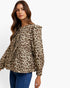 A woman wearing a beige and brown leopard print long-sleeve blouse with ruffled shoulders and a gathered waist, paired with blue jeans, against a plain white background.