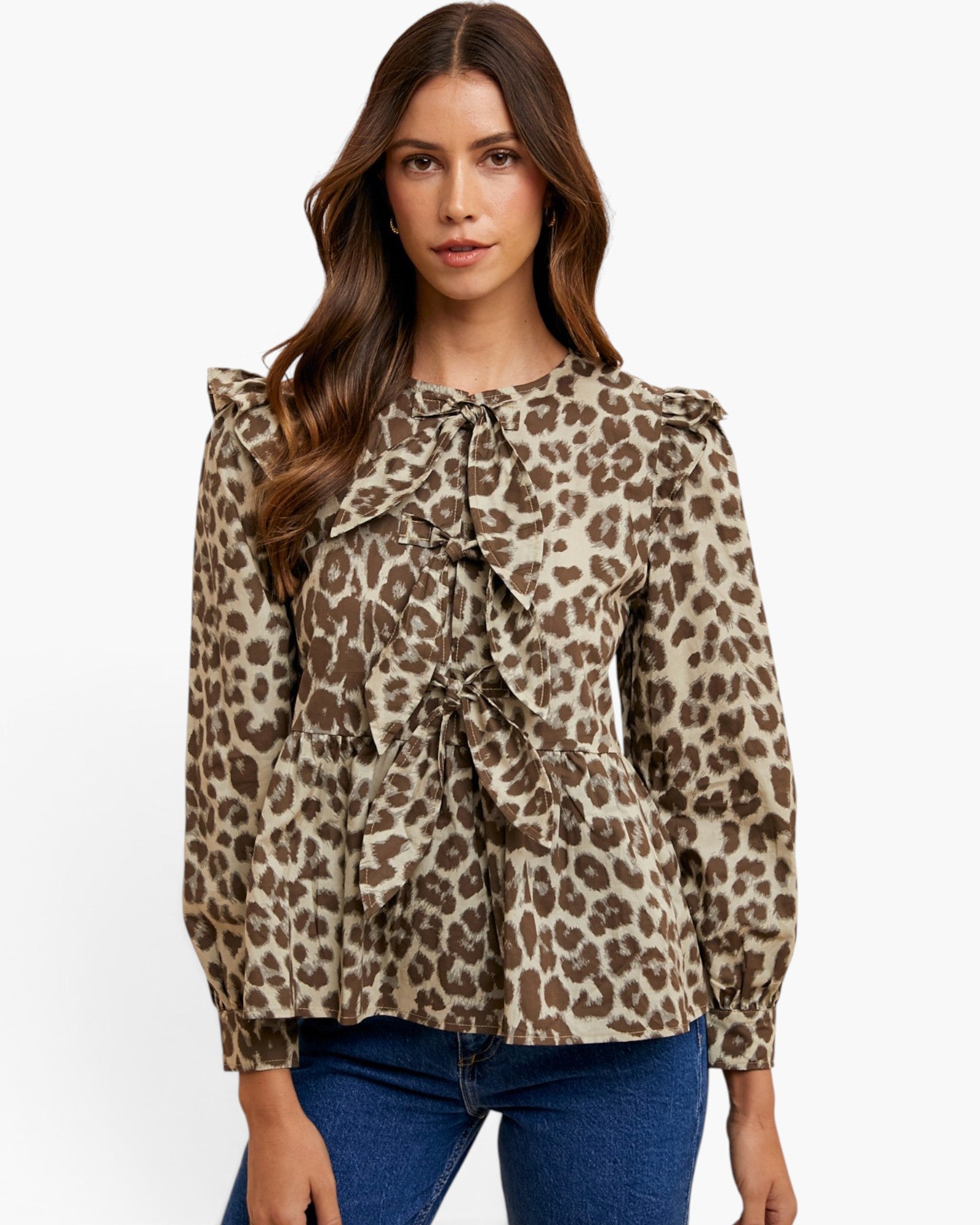 A woman modeling a long-sleeve leopard print blouse with ruffled details and a tie-neck bow, paired with blue jeans against a plain white background.
