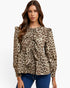 A woman modeling a long-sleeve leopard print blouse with ruffled details and a tie-neck bow, paired with blue jeans against a plain white background.